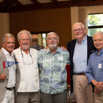Five alumni smile at the camera, one holding a Go Gaels pennant