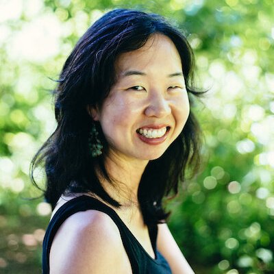 Headshot of Visiting Writer Shelley Wong smiling in front of a lush background of greenery.