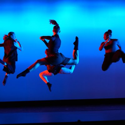 Shadowed dancers leaping in a circle with a bright blue background.