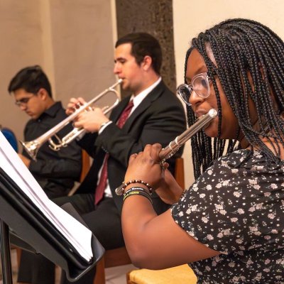 A student playing a flute and a student playing the trumpet dressed in dressy black clothes.