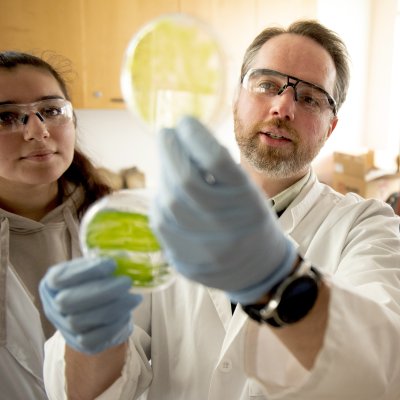 Scientist James Pesavento holds up algae in dishes while two students look on