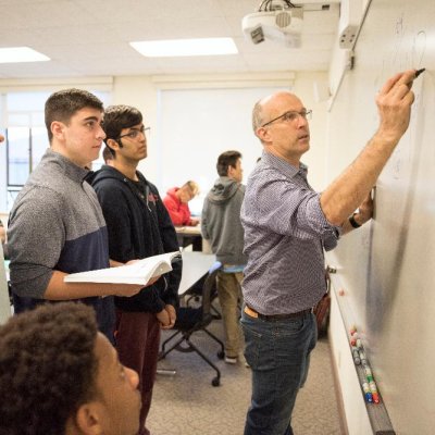 Students looking on as professor writes on whiteboard