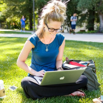 Student working on laptop while sitting on the lawn