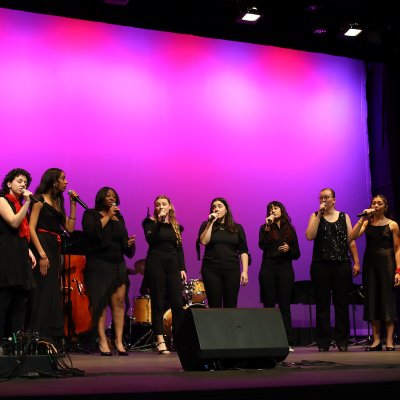 Jazz singers dressed in black with red accessories sing on LeFevre Stage with a purple hue on the cyc behind them.