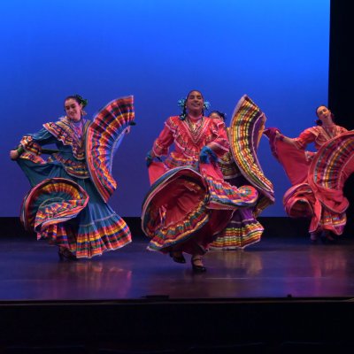 baile folklorico students dance on a stage with colorful skirts swirling around