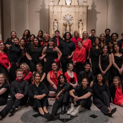SMC Choir Fall '25 with students standing and sitting in front of the altar dressed in black with red accents.