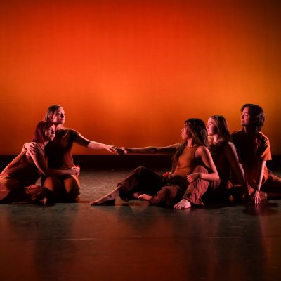 Dancers sitting on stage posed with an dark orange background
