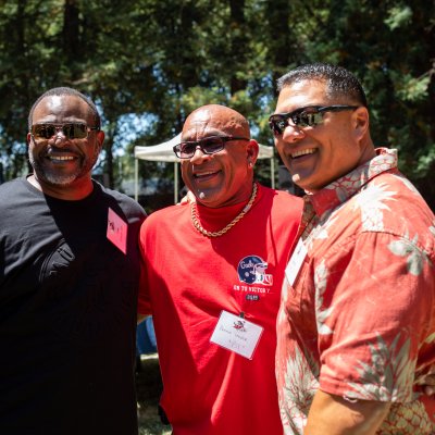 Three former football players embrace at a tailgate