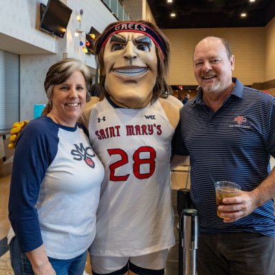 The Gael mascot poses with a couple on the concourse of a basketball rena