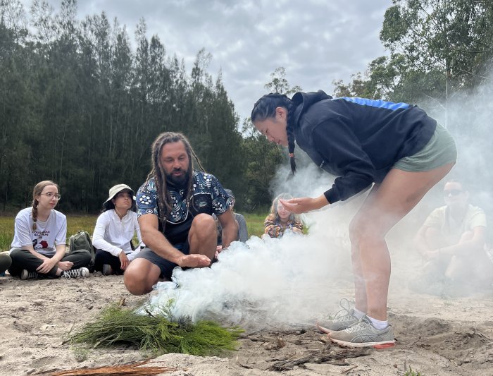 A student leans down over smoking grasses in an aboriginal custom of burning native plants to ward off bad spirits.