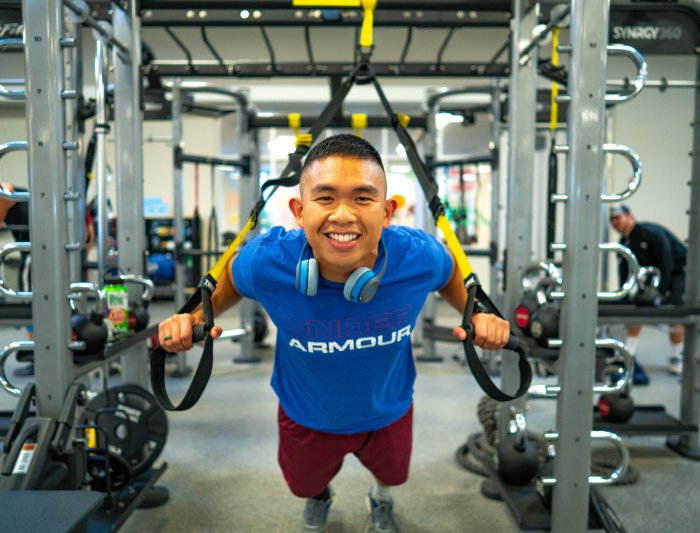 A student in the gym on a trx machine leaning in and smiling