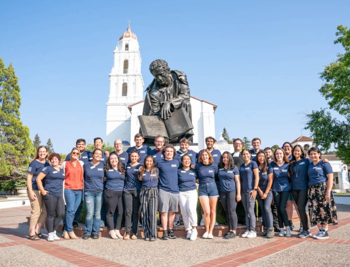 A group of Mission and Ministry workers posing in front of a chapel and a statue