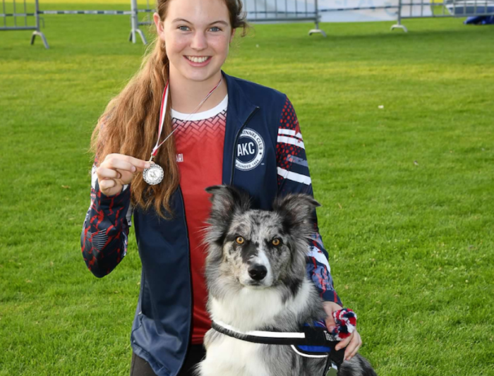 A student holding a medal and posing with her dog