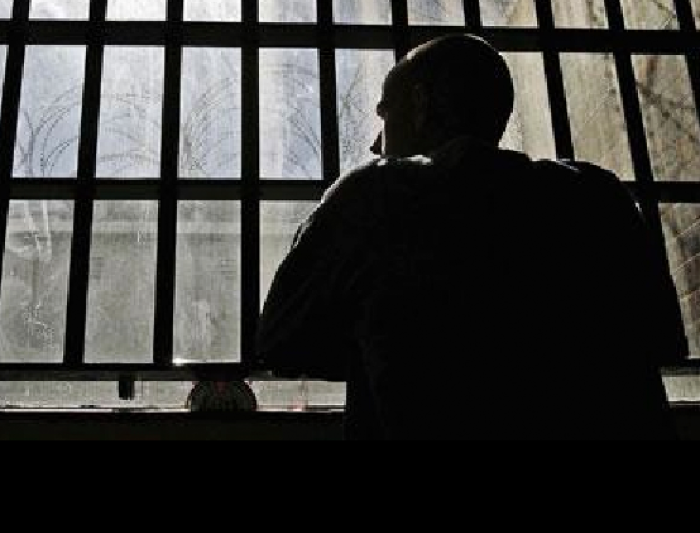 An incarcerated man looking out the bars in a window