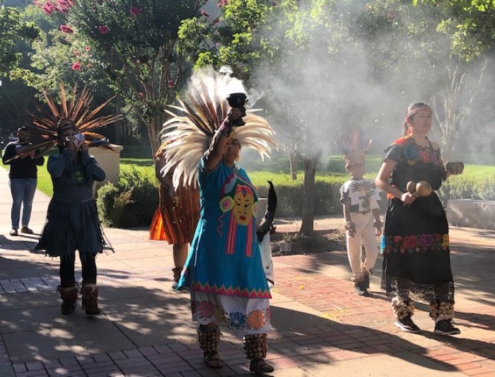 Women in traditional indigenous clothing hold a cup with incense on campus