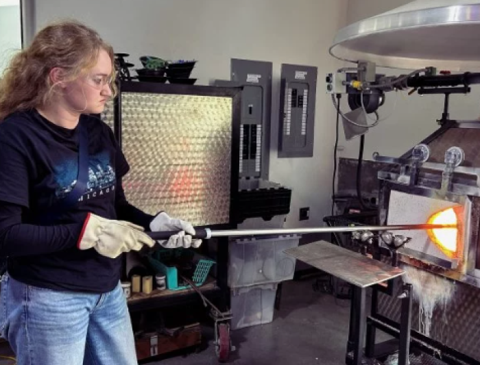 Experiencing the heat firsthand, Maggie Vance '27 preps the rod at the furnace in the Mare Island hot shop. / Photo courtesy Campus Recreation