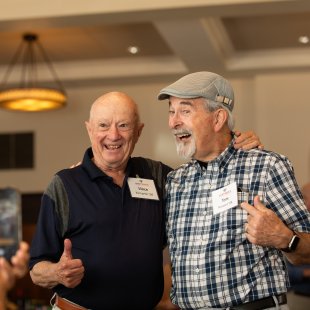 Two older male alumni smile theatrically for a photo