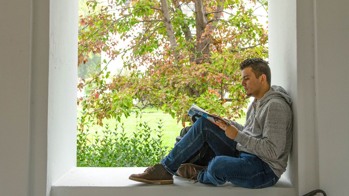 Student reads while sitting on a window seal