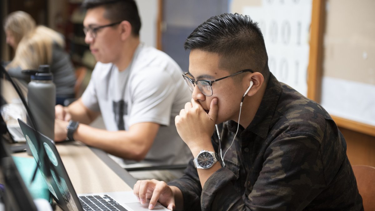 A student working on a computer with ear buds in 