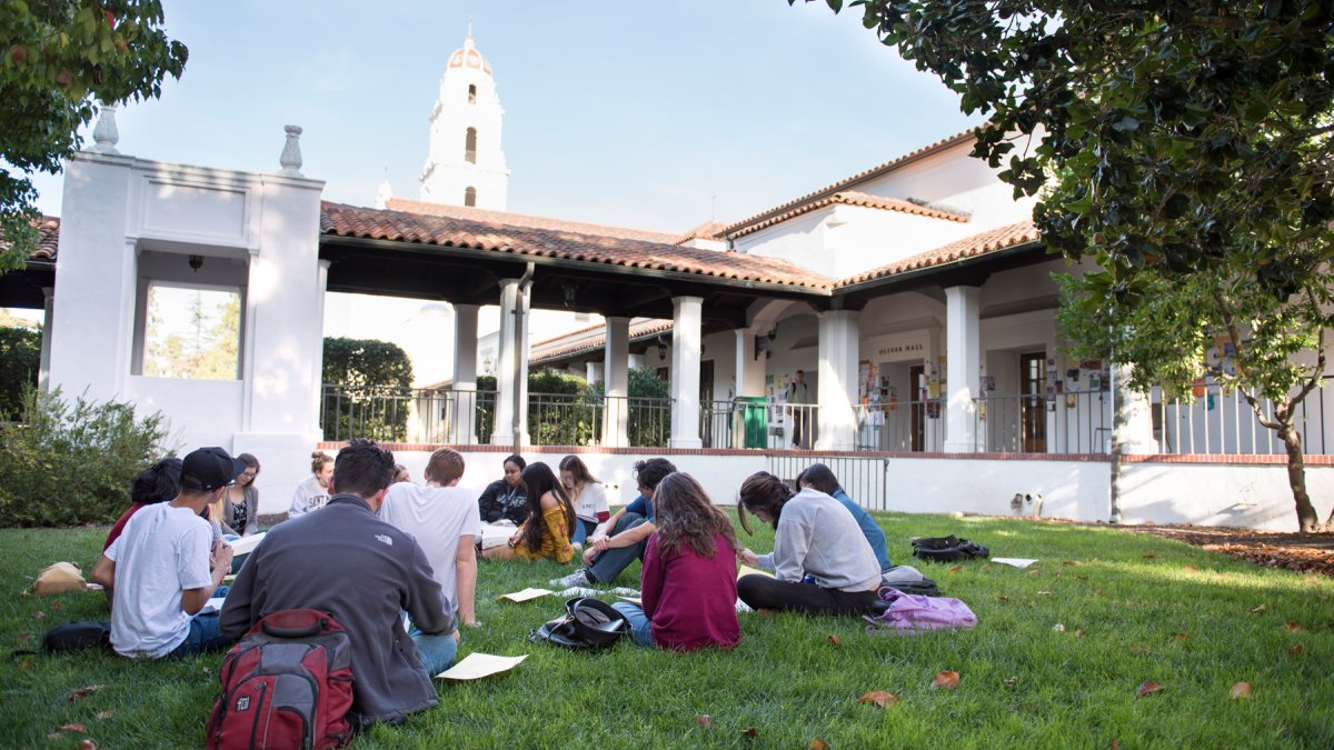 A class meeting outside on the grass with the SMC chapel in the background