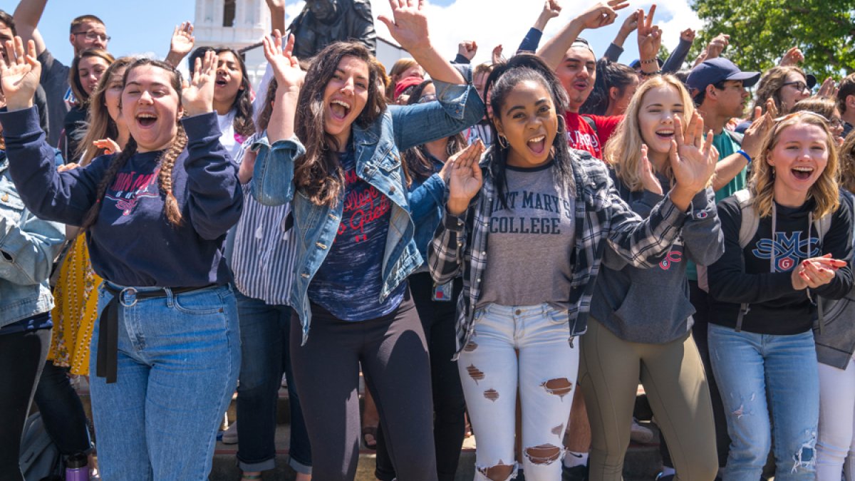 Students smiling and cheering with their hands up in front of the Saint Mary's College Chapel