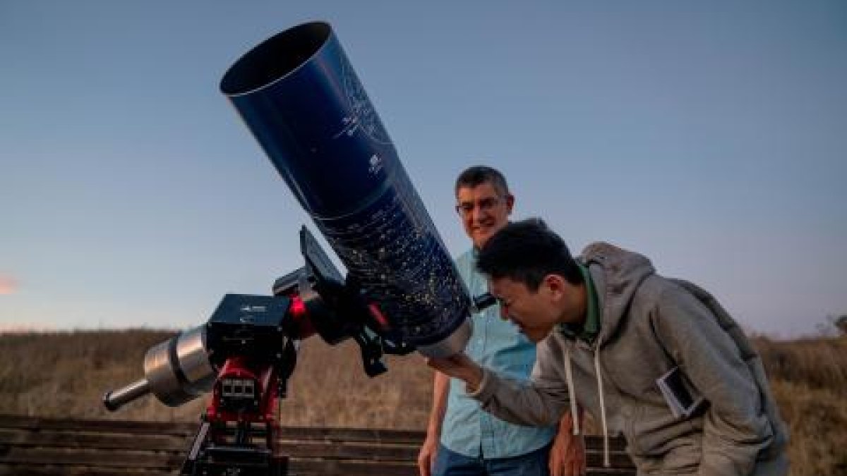 Student viewing night sky with large telescope as faculty looks on