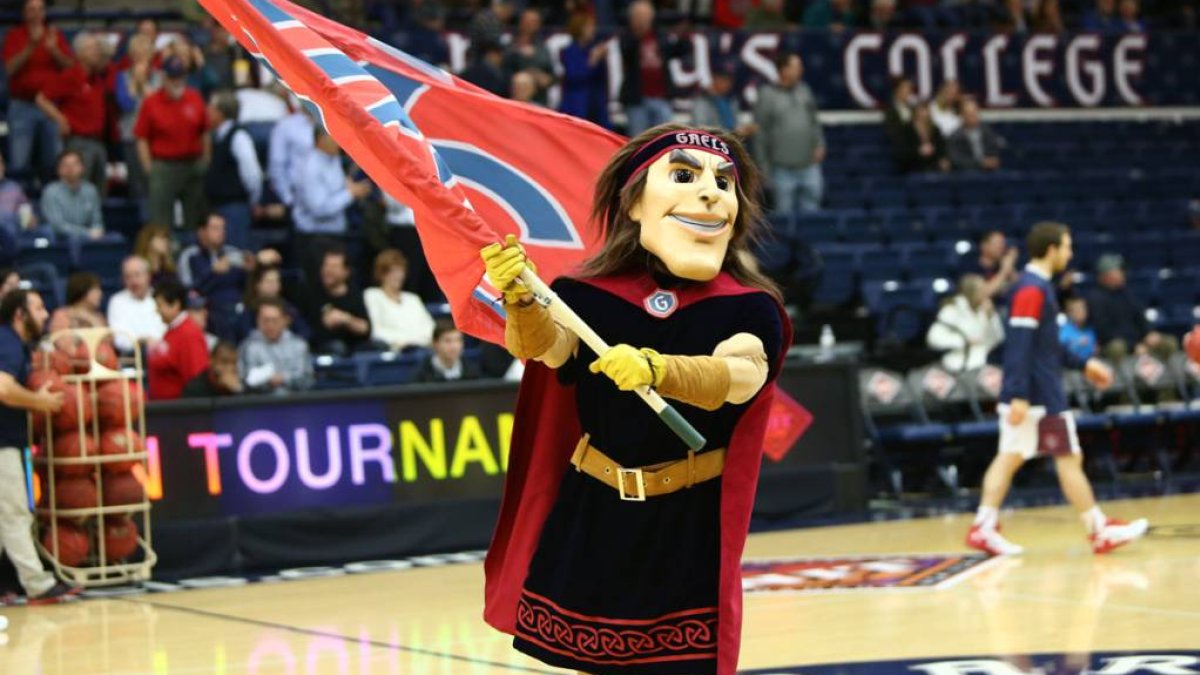 Gideon the SMC mascot running across the basketball court holding a flag
