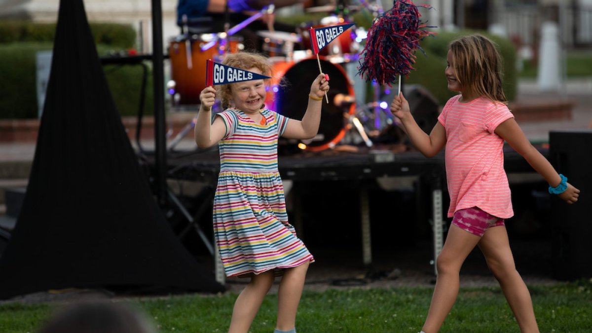 Two school-aged girls wave pom poms and pennants