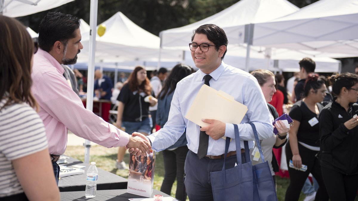 A student in a tie smiling and shaking hands with a man