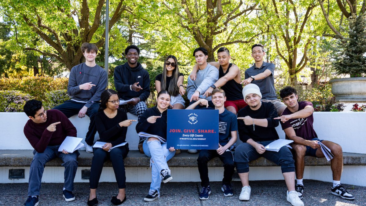 A dozen students point at a One Day One SMC sign on campus