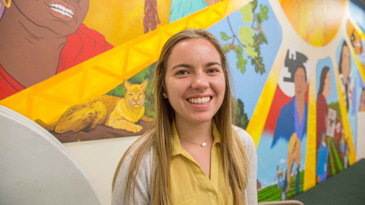 Student smiling in front of mural