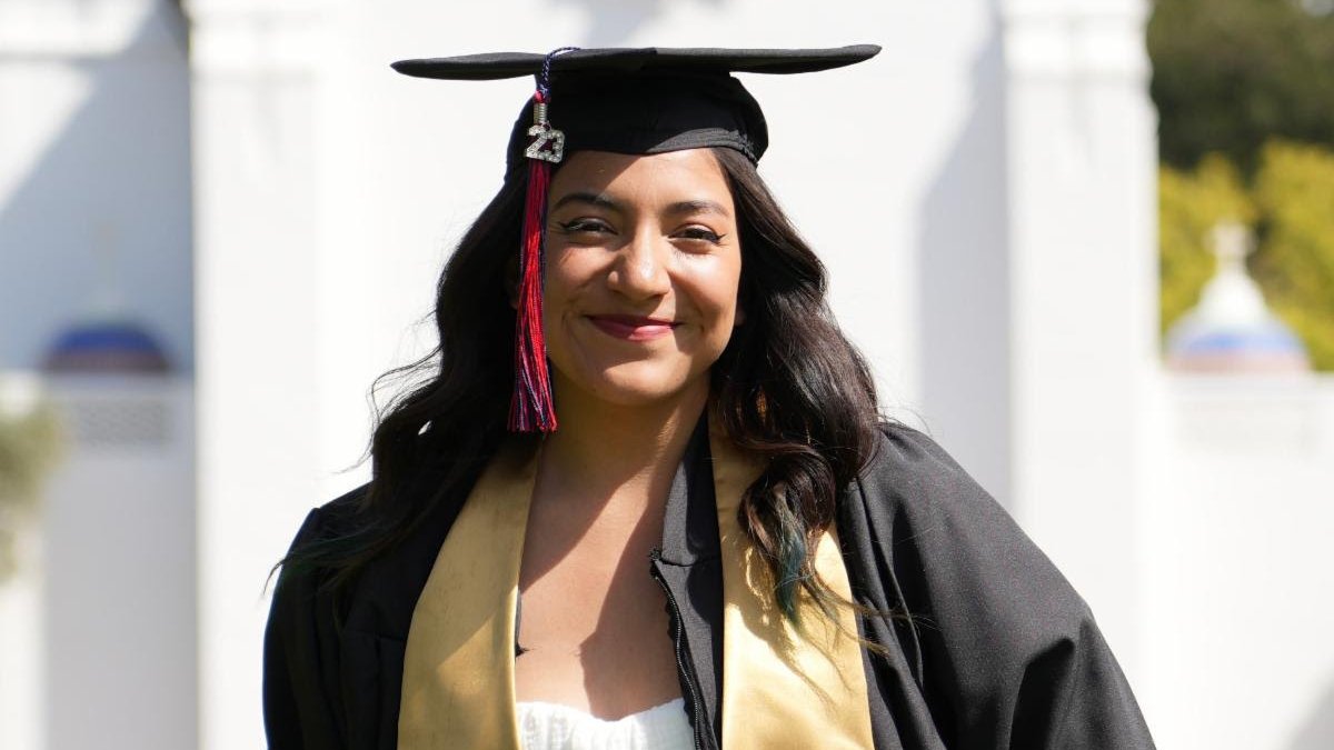 Graduation photo of Miranda Vega, MA in Comm alumni in robes/garb.