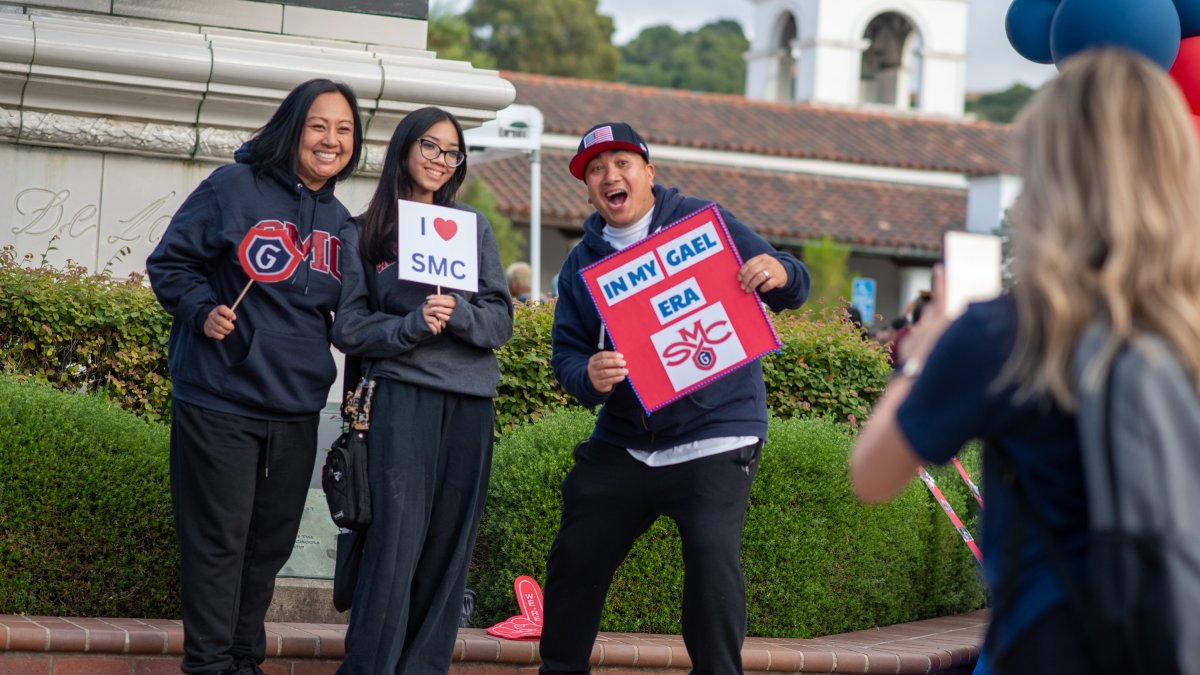 Three individuals stand together Gael themed signs